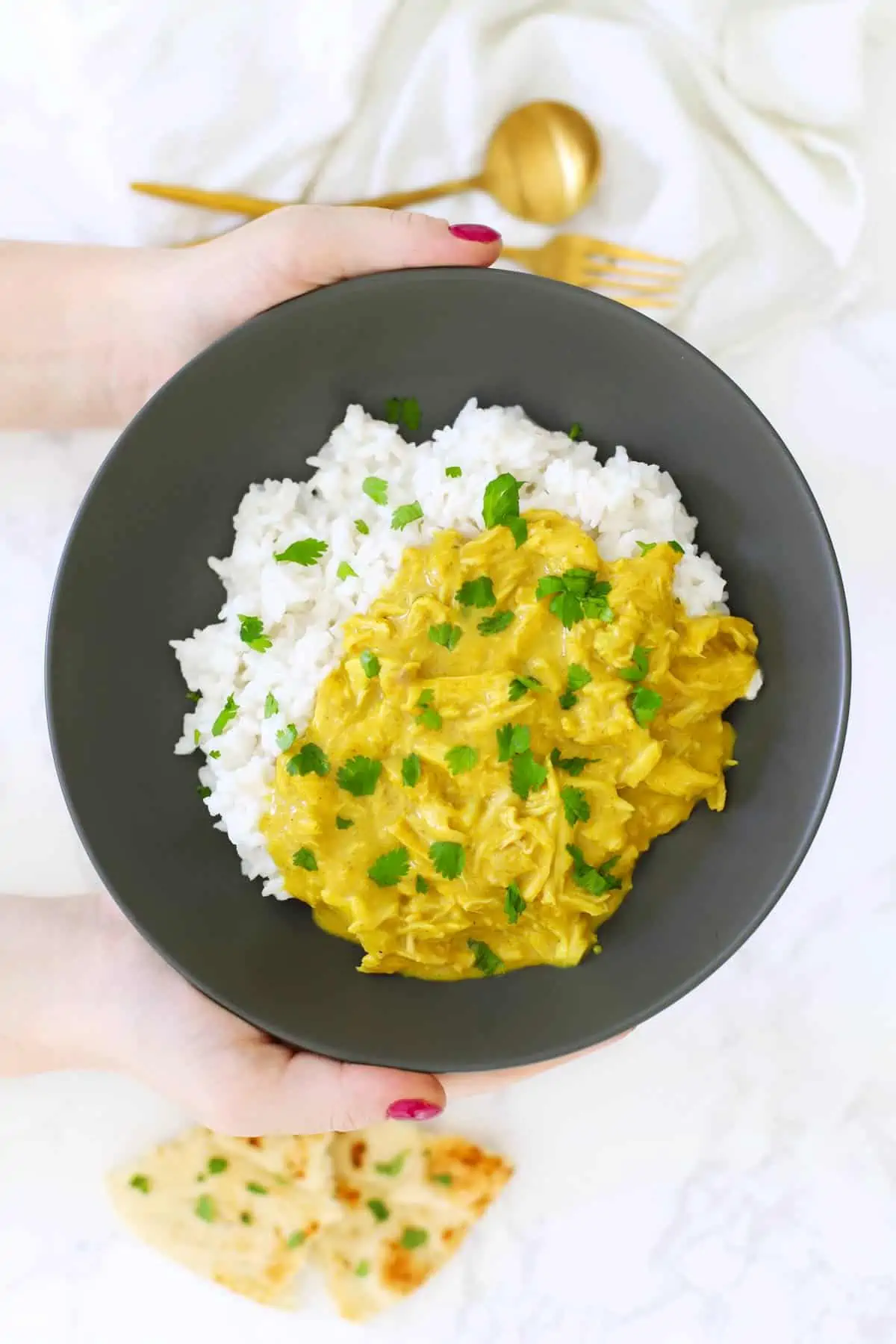 Two hands holding a dark grey bowl of shredded curry chicken. 