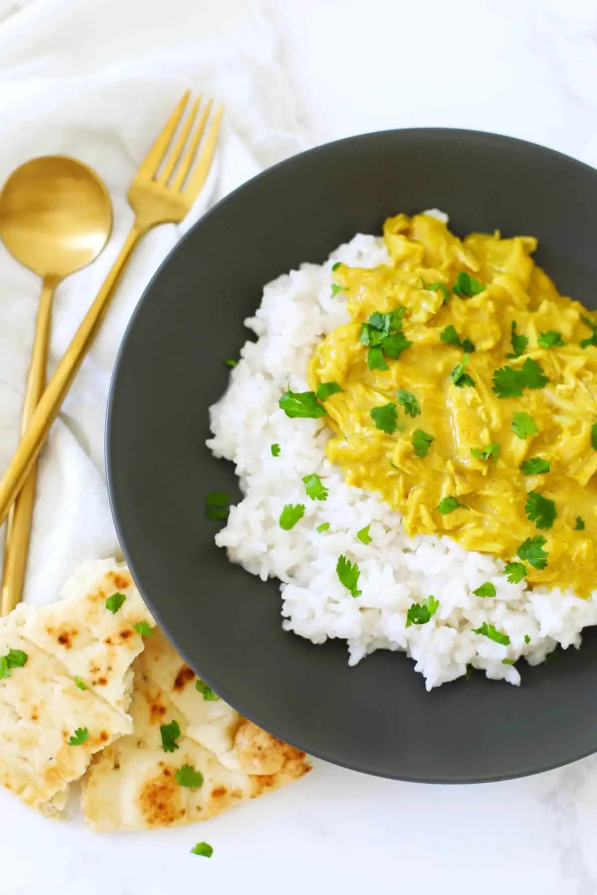 Shredded curry chicken with coconut rice on a black plate. 