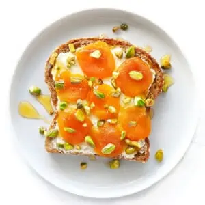 Toast on a white plate with apricots and honey.