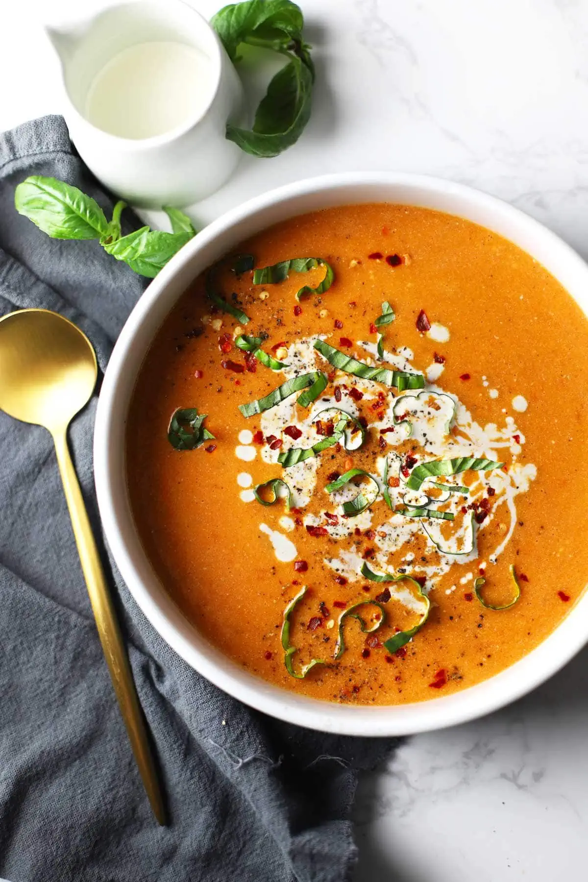 Tomato basil soup in a white bowl with a gold spoon. 