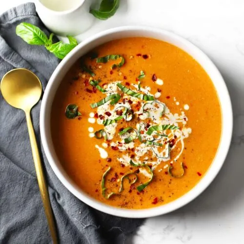 Tomato soup in a white bowl topped with basil.