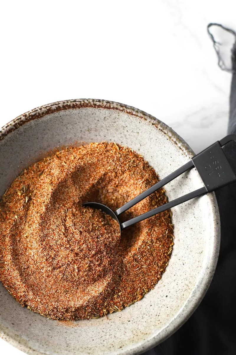 Cajun seasoning in a grey bowl with black measuring spoon. 