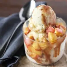 Vanilla ice cream with cinnamon apple topping in a clear glass on grey napkin.