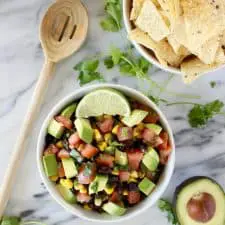 Black beans, corn, tomato and avocado in white bowl.