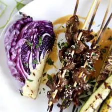 Beef skewers, grilled vegetables and peanut sauce on white plate.