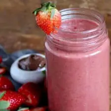 Pink smoothie in mason jar on wood surface.