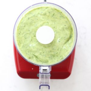 Green sauce in glass bottle on white surface.