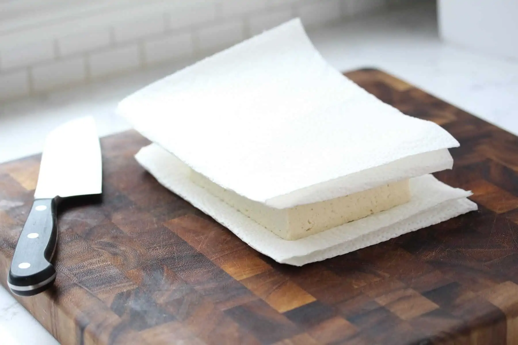 Tofu wrapped in paper towels on cutting board.