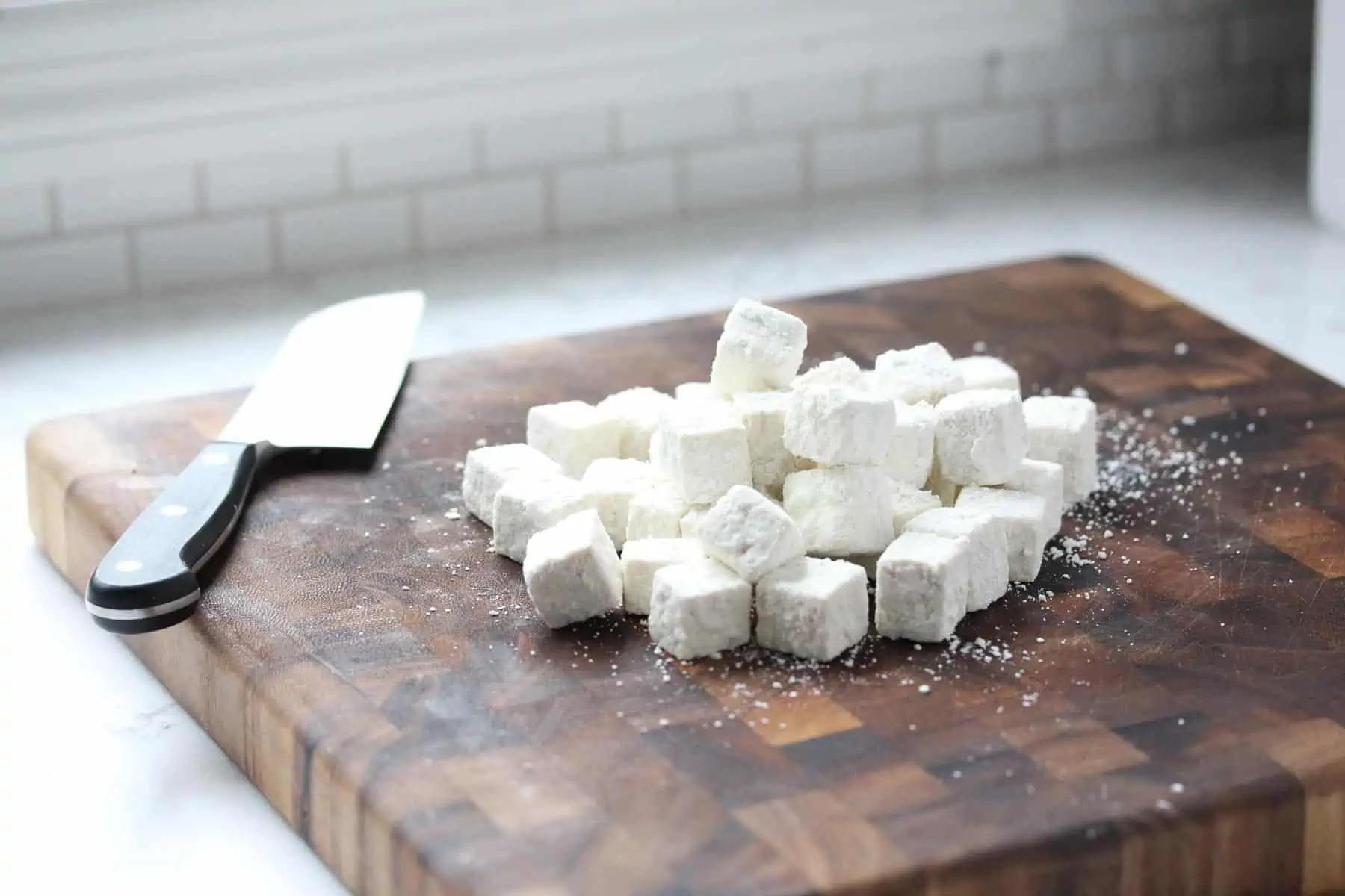 Cubed tofu coated in corn starch on cutting board.