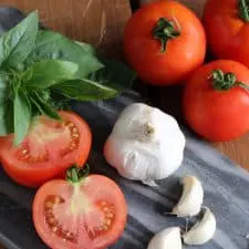 Tomatoes, basil, garlic and onion on blue cutting board.