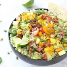 Guacamole in black bowl with corn, tomatoes, jalapeños and bacon