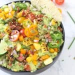 Guacamole in black bowl with corn, tomatoes, jalapeños and bacon