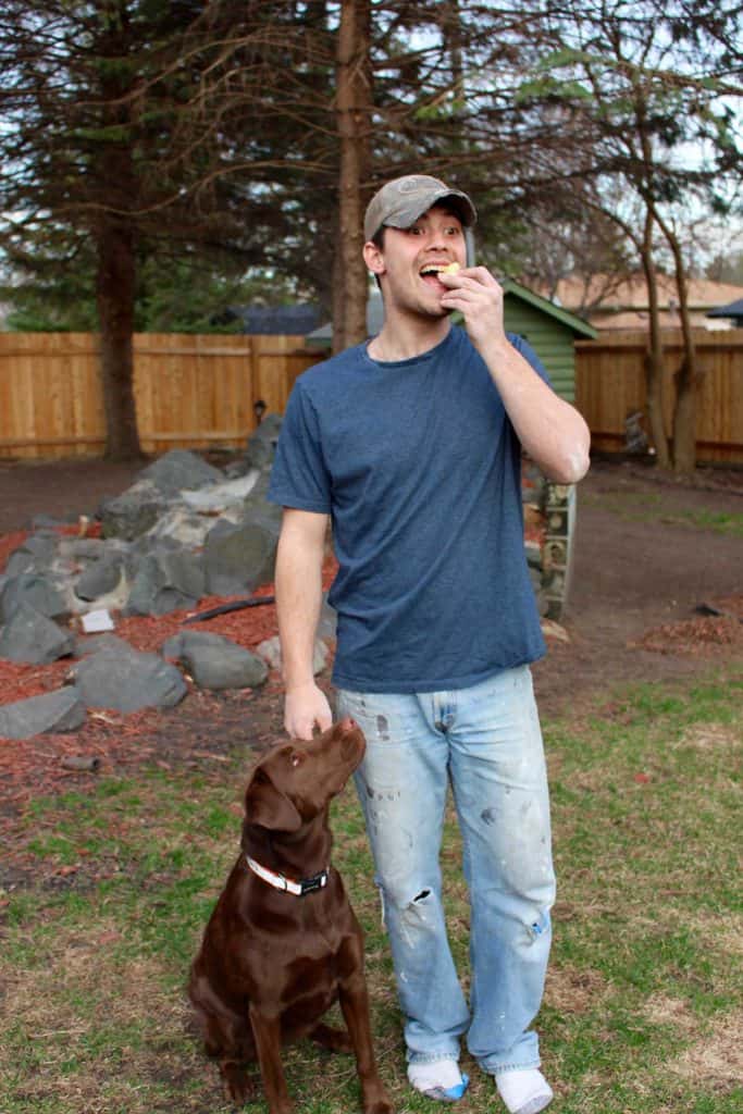Man eating hard boiled egg next to dog.