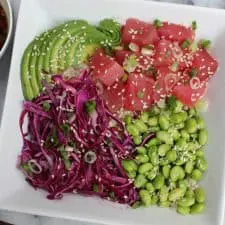 Raw tuna, edamame, avocado and cabbage in white bowl.