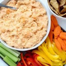 Buffalo dip in white bowl with sliced vegetables.