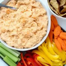 Buffalo dip in white bowl with sliced vegetables.