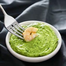 Shrimp on fork dipped in green sauce in white bowl.