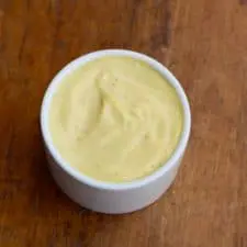 Hollandaise in white bowl on wood surface.