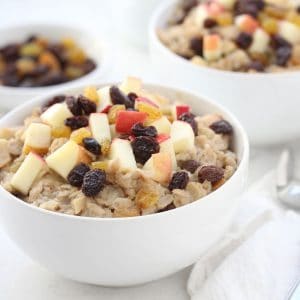 Apple raisin oatmeal in white bowl with two spoons.