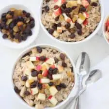 Apple raisin oatmeal in white bowl with two spoons.