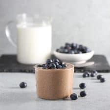 Chocolate pudding in glass on grey surface with blueberries.