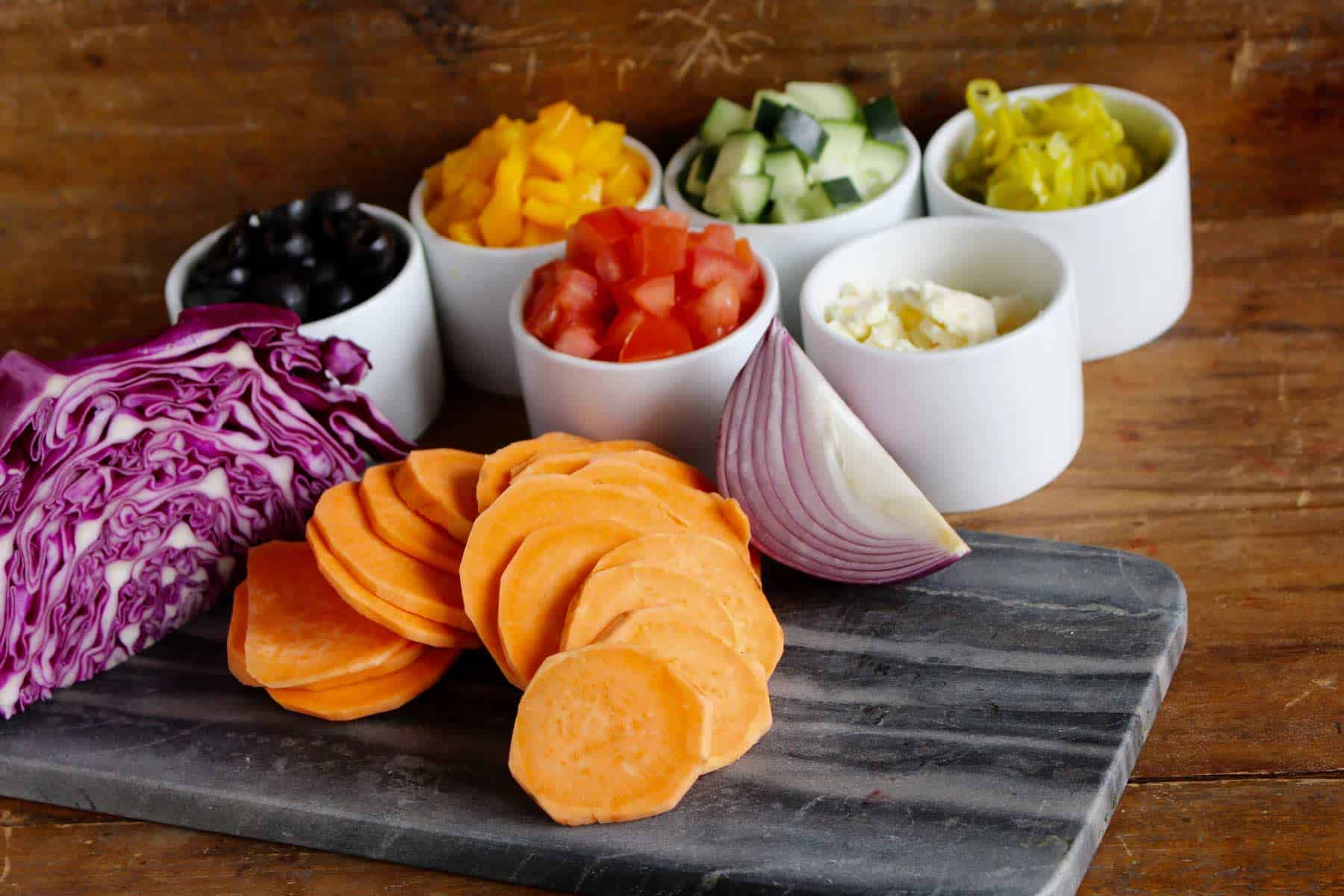 Vegetables in white bowls on a grey cutting board.