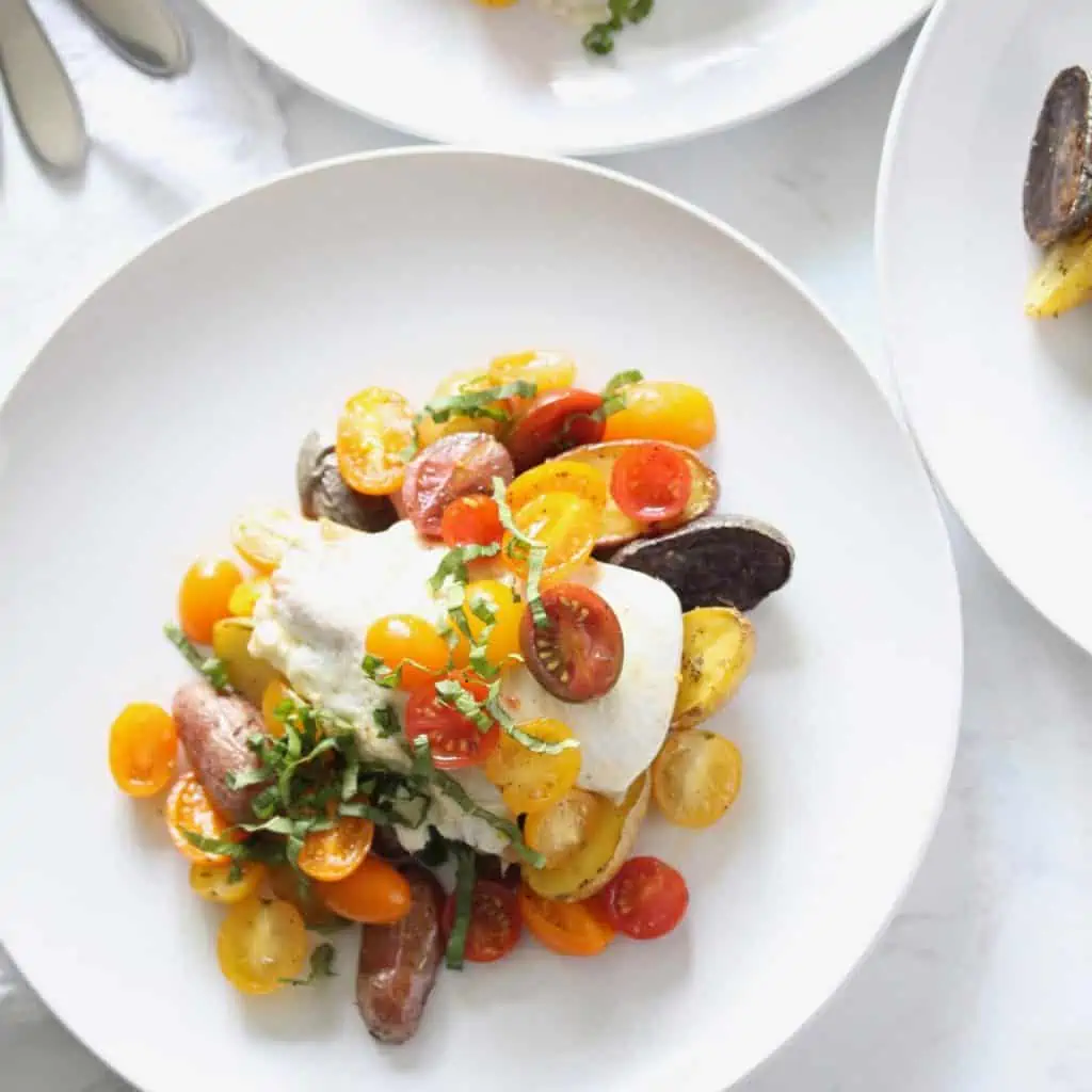 Chicken with tomatoes and potatoes on white plate.