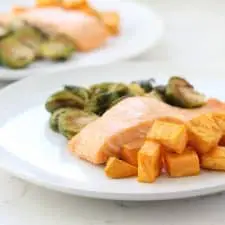 Salmon, sweet potatoes and Brussels sprouts on white plate.