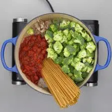 Spaghetti ingredients in blue pot on grey background.