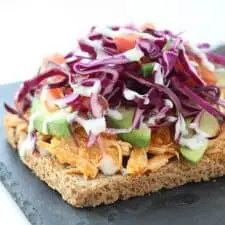 Open face buffalo chicken sandwich on grey stone cutting board.