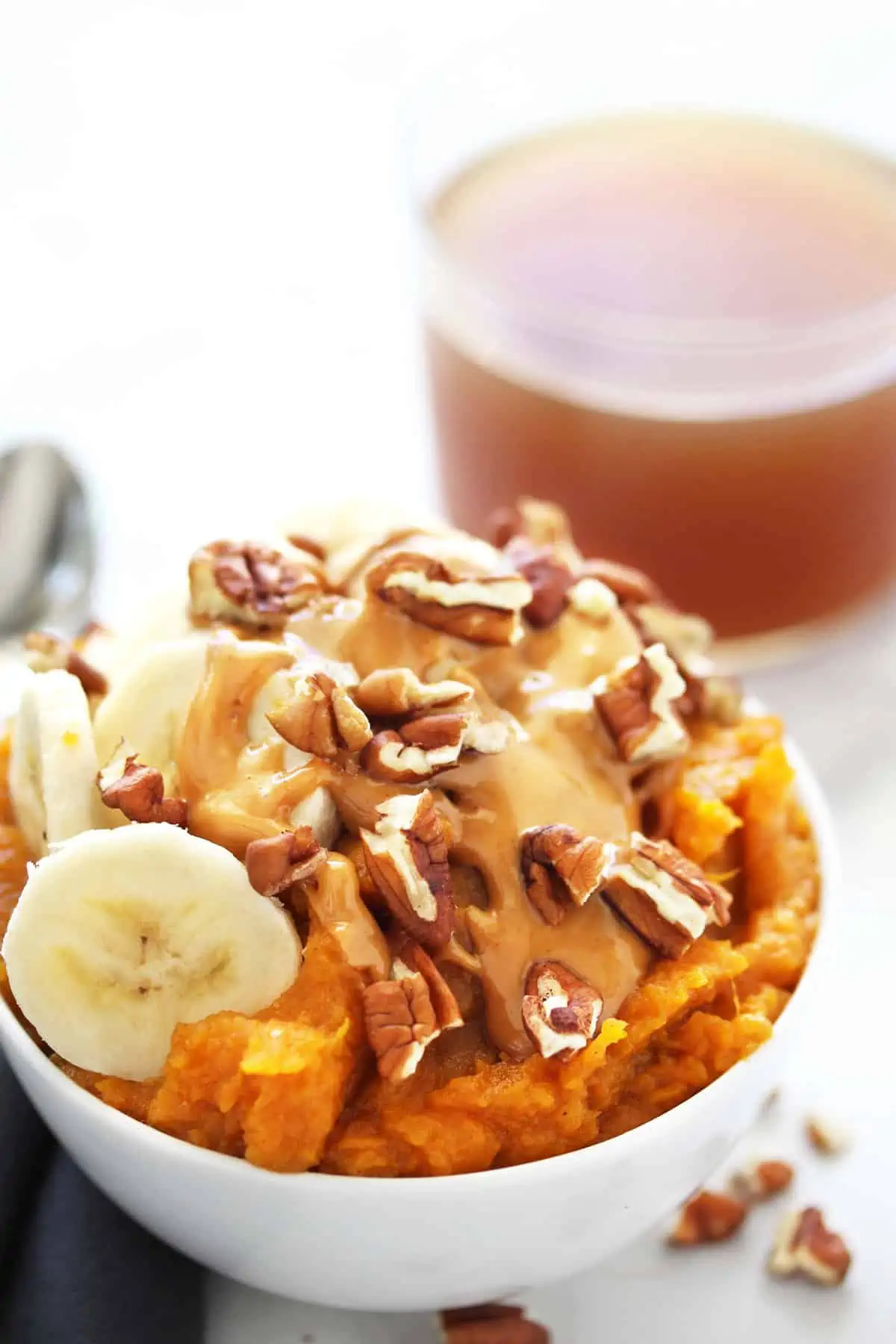 Sweet potatoes with banana slices, peanut butter and walnuts in a white bowl on grey napkin.