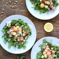 Salad on three white plates on wood surface.