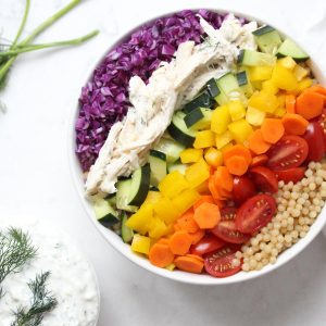 Fresh veggies, couscous and chicken in white bowl with Tzatziki sauce.