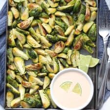 Roasted Brussels sprouts on sheet pan with bowl of aioli.