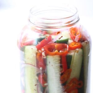 Pickles and peppers in clear mason jar on white surface.