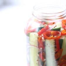 Pickles and peppers in clear mason jar on white surface.