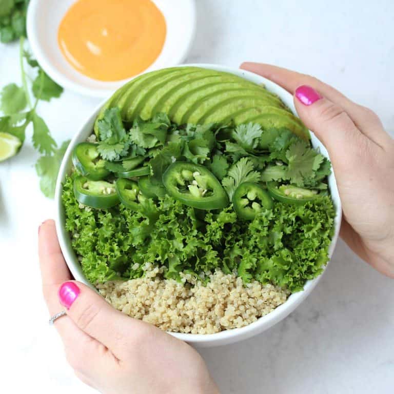Hands holding a grain salad in white bowl.
