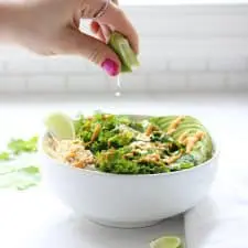 Hand squeezing lime over green grain bowl.
