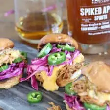 Pork sliders on grey cutting board with whiskey bottle.