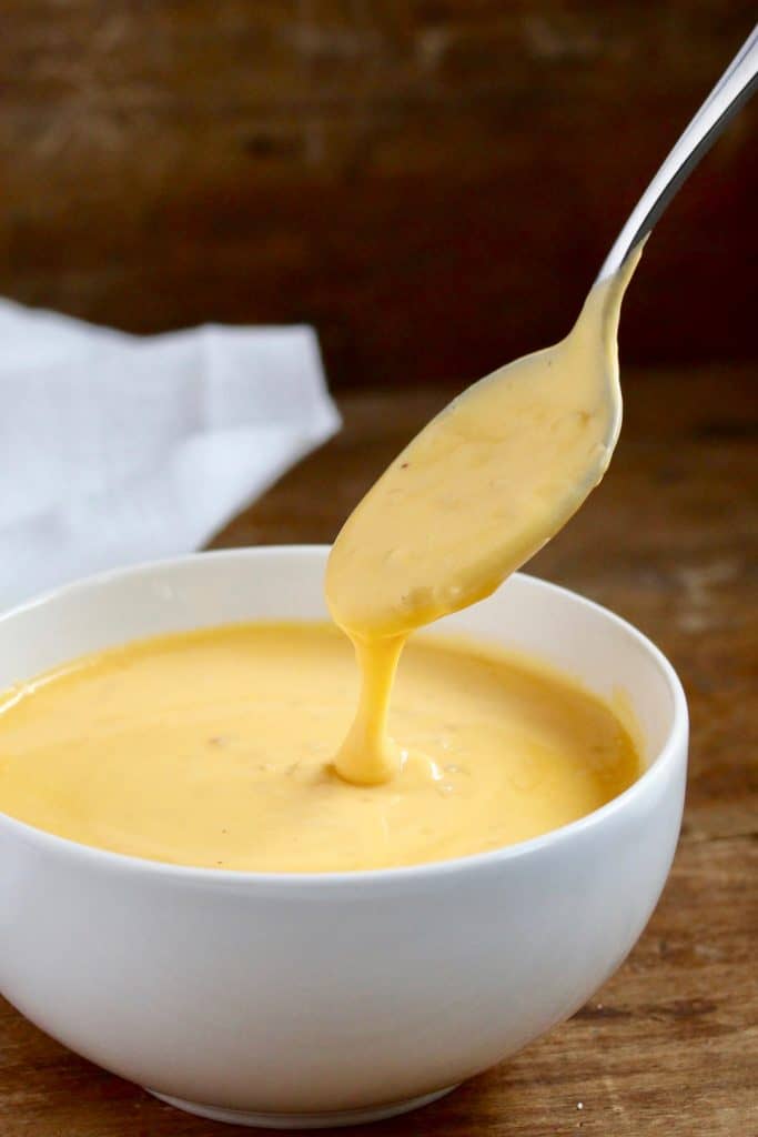 Spoon pouring cheese sauce in white bowl.