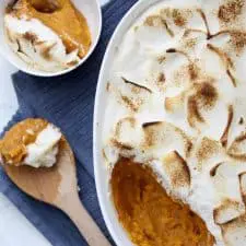 Sweet potato casserole in white dish with spoon and blue napkin.