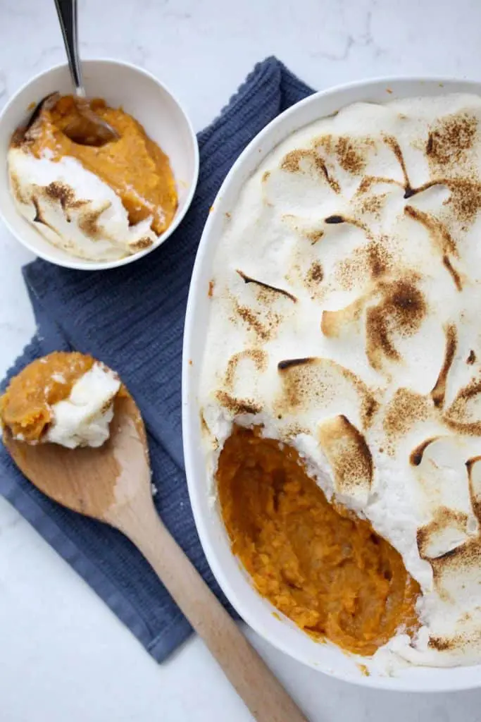 Sweet potato casserole in white dish with spoon and blue napkin.