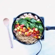 Pasta ingredients in pan on white surface with wood spoon.