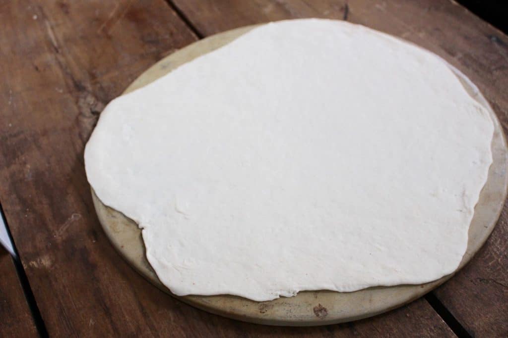 Pizza dough rolled out on pizza stone.