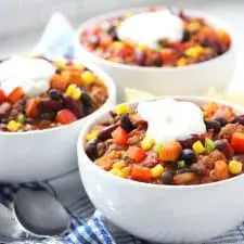 Chili in white bowls on blue plaid napkins.